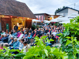 Eine große Menschenmenge sitzt bei einem Veranstaltungsort im Freien und lauscht.