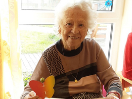 Eine ältere Frau lächelt und hält einen bunten Papier-Schmetterling in der Hand.