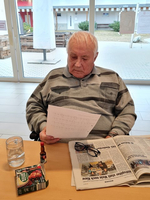 Älterer Mann liest ein Blatt Papier, während er an einem Tisch sitzt.