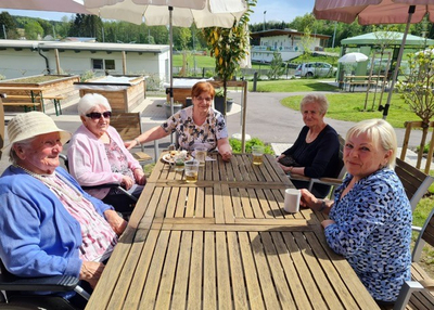 Fünf Frauen sitzen entspannt an einem Tisch im Freien.