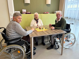 Drei Senioren sitzen an einem Tisch und spielen ein Brettspiel.