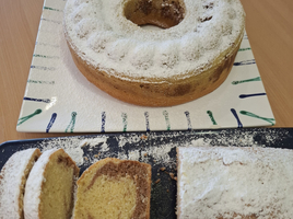 Ein runder, geschnittener Kuchen, bestäubt mit Puderzucker, liegt auf einem Teller.