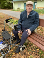 Ein älterer Mann sitzt auf einerBank neben einem Rollator im Herbst.