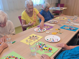 Ältere Frauen gestalten kreative Bastelarbeiten mit bunten Perlen am Tisch.
