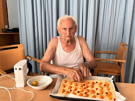 Ein älterer Mann bereitet einen Obstkuchen in einer Küche vor.