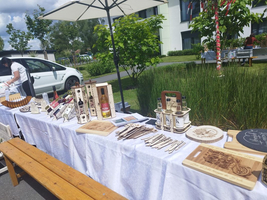Ein Marktstand mit handgefertigten Holzprodukten und Getränken unter einem Sonnenschirm.