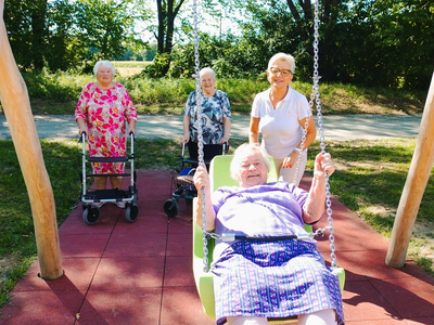 Ältere Frauen im Freien auf einer Schaukel und mit Rollatoren.