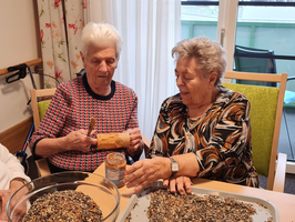 Zwei ältere Frauen bereiten gemeinsam Vogel-Futter aus Samen und Erdnussbutter vor.