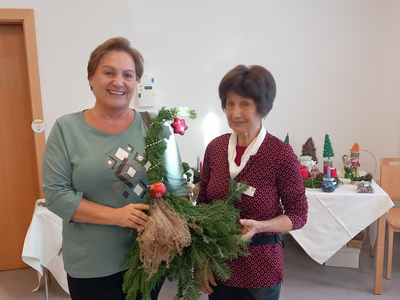 Zwei Frauen halten einen Weihnachtskranz in einem festlich dekorierten Raum.