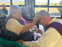 Ein Priester segnet eine ältere Frau während einer Feier in einem Raum.