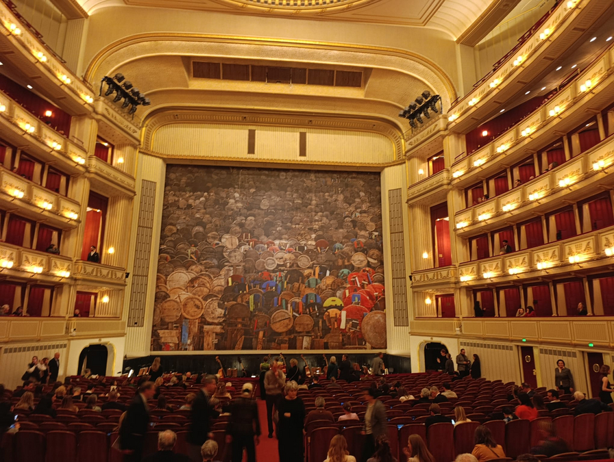 Eine elegante Theaterbühne mit einem künstlerischen Hintergrund und Zuschauern im Publikum.