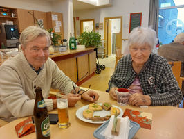 Ein älteres Paar sitzt an einem Tisch mit Snacks und Getränken.