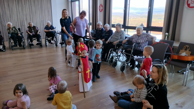 Kinder tanzen und singen mit Senioren in einem Gemeinschaftsraum.