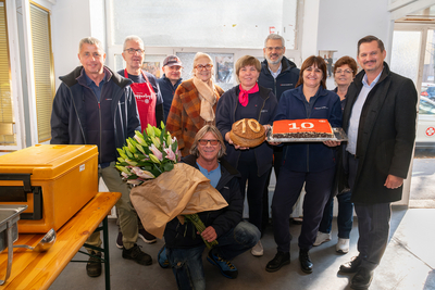 Gruppenbild mit Blumen und Torte im Sozialmarkt Gellertgasse. Mit freiwilligen Helfern, hauptamtlichen Kräften, Bezirksvorsteher Marcus Franz, Susanne Drapalik und Oliver Löhlein