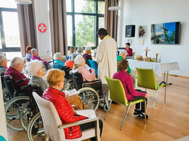 Eine Gruppe von Senioren nimmt an einer Zeremonie in einem Gemeinschaftsraum teil.
