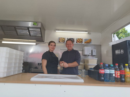 Zwei Personen stehen lächelnd an einem Foodtruck mit Getränken und Lebensmitteln.