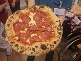 Eine Person in Uniform hält eine Pizza mit Salami hoch.