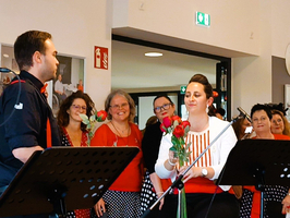 Ein Sänger übergibt einer Frau mit Rosen Blumen, umgeben von applaudierenden Zuhörern.