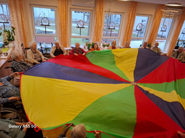 Senioren spielen gemeinsam mit einem bunten Fallschirm in einem Gemeinschaftsraum.
