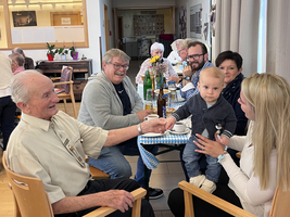 Familienmitglieder sitzen zusammen, ein älterer Mann hält ein Kind auf dem Schoß.