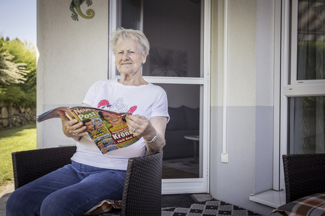 Eine ältere Frau sitzt auf der Terrasse und liest eine Zeitschrift.