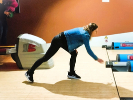 Eine Person spielt Bowling und wirft den Ball in Richtung der Bahn.