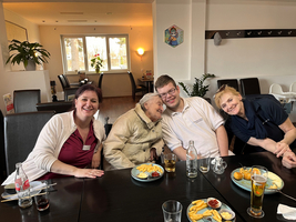 Vier Personen lächeln gemeinsam an einem Tisch mit Essen und Getränken.