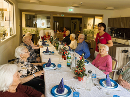 Weihnachtsfeier mit älteren Menschen an festlich gedecktem Tisch in einem Gemeinschaftsraum.