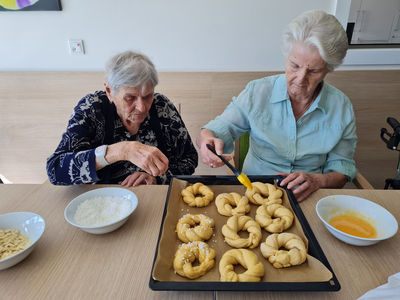 Zwei ältere Frauen bereiten frisch gebackene Brötchen auf einem Tisch vor.