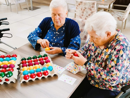 Zwei Frauen bemalen bunte Ostereier am Tisch.