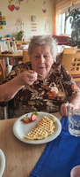 Eine ältere Frau genießt Waffeln mit Erdbeeren in einem gemütlichen Raum.