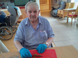 Älterer Mann in Handschuhen schneidet Limetten auf einem roten Brett.