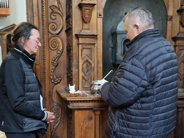 Zwei Personen stehen an einem holzverzierten Schalter und sprechen miteinander.