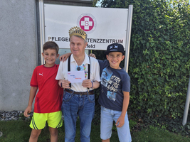 Drei Jungen stehen lächelnd zusammen vor einem Schild mit dem Text 