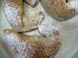 Drei gebackene Croissants, bestreut mit Puderzucker, auf einem Teller.