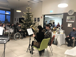 Weihnachtsfeier mit Musikern vor einem geschmückten Baum und Gästen.