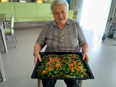 Eine ältere Frau hält ein Tablett mit frischem Salat in den Händen.