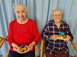 Zwei ältere Menschen lächeln mit ostertafeln und bunten Eiern in der Hand.