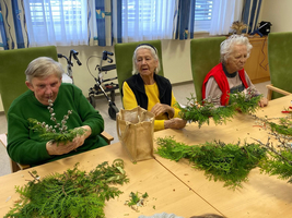 Drei ältere Menschen gestalten mit Pflanzenarrangements an einem Tisch.