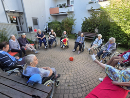 Ältere Menschen im Rollstuhl sitzen im Kreis in einem Garten.