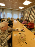 Ältere Menschen spielen Bingo an einem Tisch in einem Gemeinschaftsraum.