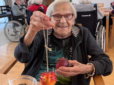 Eine ältere Frau hält eine hängende Frucht und eine weitere Frucht in der Hand.