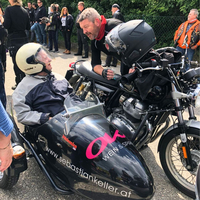Ein Mann spricht mit einem älteren Fahrer im Beiwagen eines Motorrads.