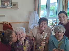 Fünf Personen lächeln glücklich und halten kleine Glasvasen mit Blumen.