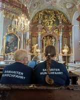 Zwei Personen mit „Samariter Wunschfahrt“-Shirts sitzen in einer Kirche.