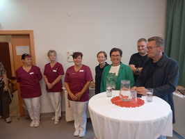Gruppenfoto von Mitarbeitern in Uniform und einer Person am Tisch, die spricht.