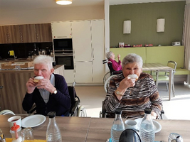 Zwei ältere Menschen in Rollstühlen trinken Kaffee in einem Gemeinschaftsraum.