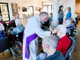 Ein Priester segnet Bewohner in Rollstühlen in einem Altersheim.