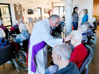 Ein Priester segnet Bewohner in Rollstühlen in einem Altersheim.