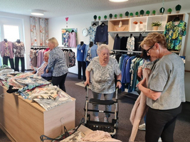 Seniorinnen betrachten Kleidung in einem Geschäft, einige sitzen, andere stehen mit Rollator.